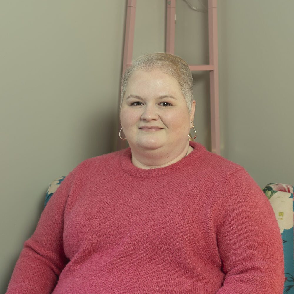 Therapist sitting in blue chair with floral pattern wearing a pink sweater