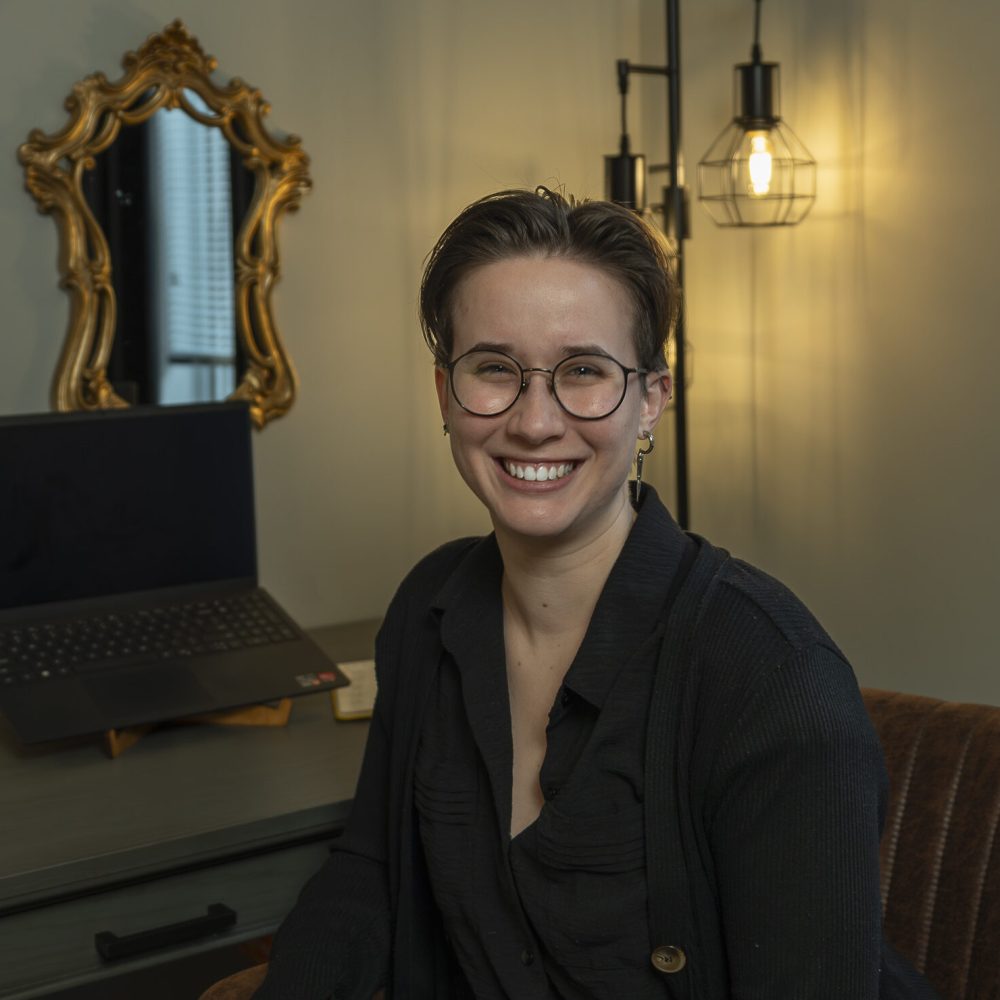 Therapist smiling in front of desk with laptop, mirror, and lamp behing them